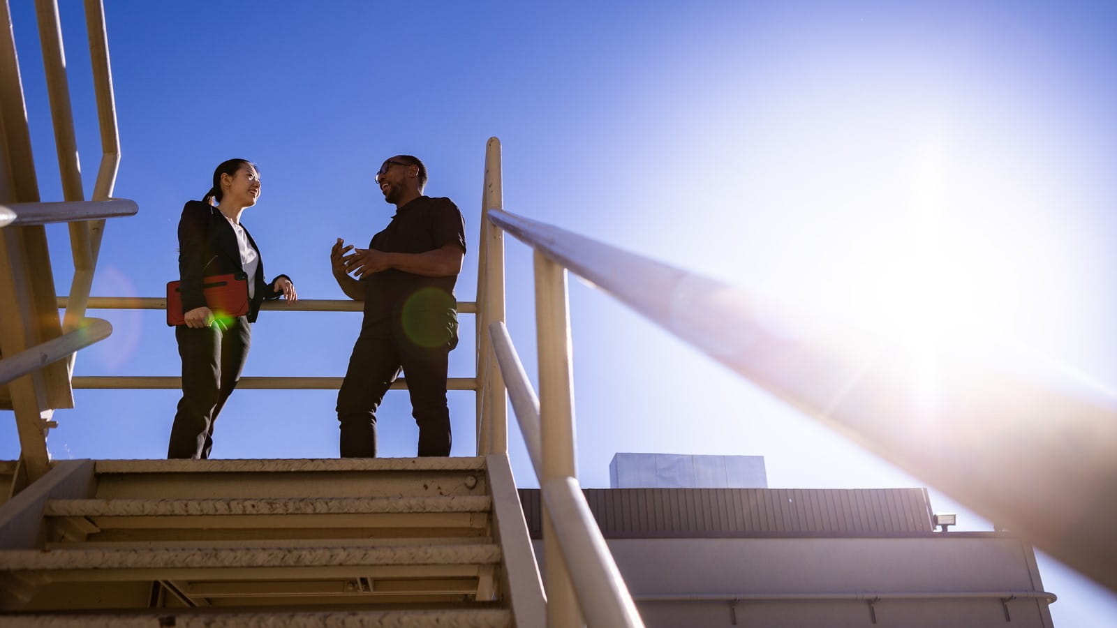 Adult male and adult female having a conversation at the top of a staircase outside on a clear day. 