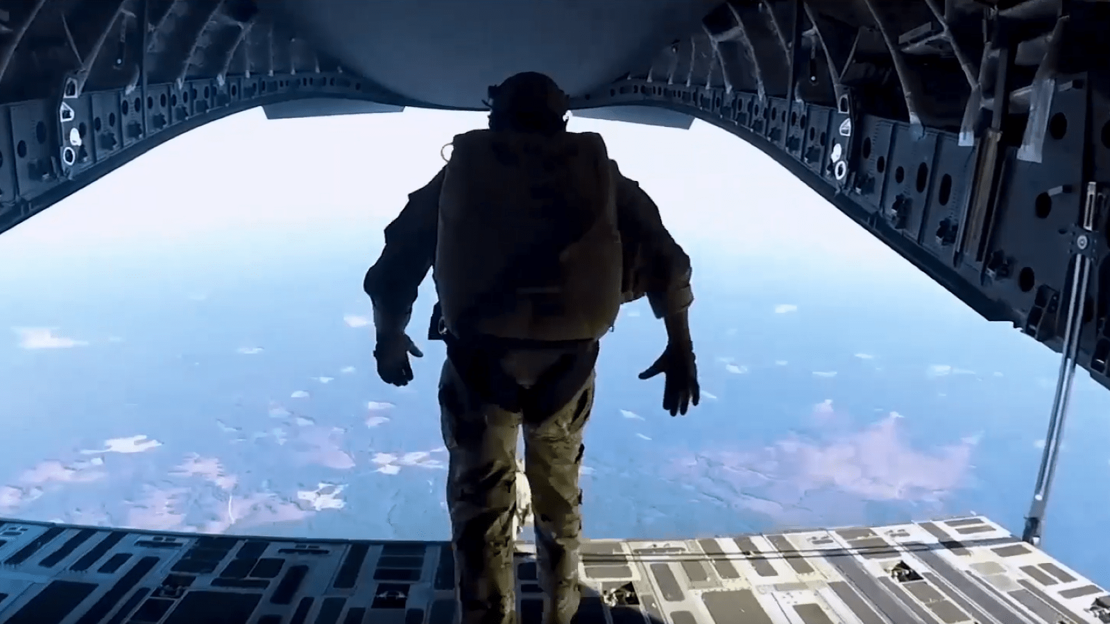 View from behind of a military service member approaching a jump from the back of a plane in the air.